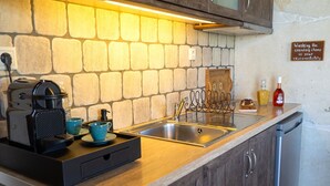 Una cocina con protector de salpicadero de piedra, una cafetera, un lavamanos con grifo decorativo y un cartel sobre el lavado de utensilios de cocina.