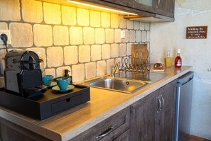 A kitchen with a stone backsplash, a coffee machine, a sink with a decorative faucet, and a sign about washing cooking items.