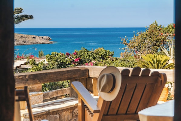 A wooden chair with a hat, overlooking a coastal view with a clear sky.