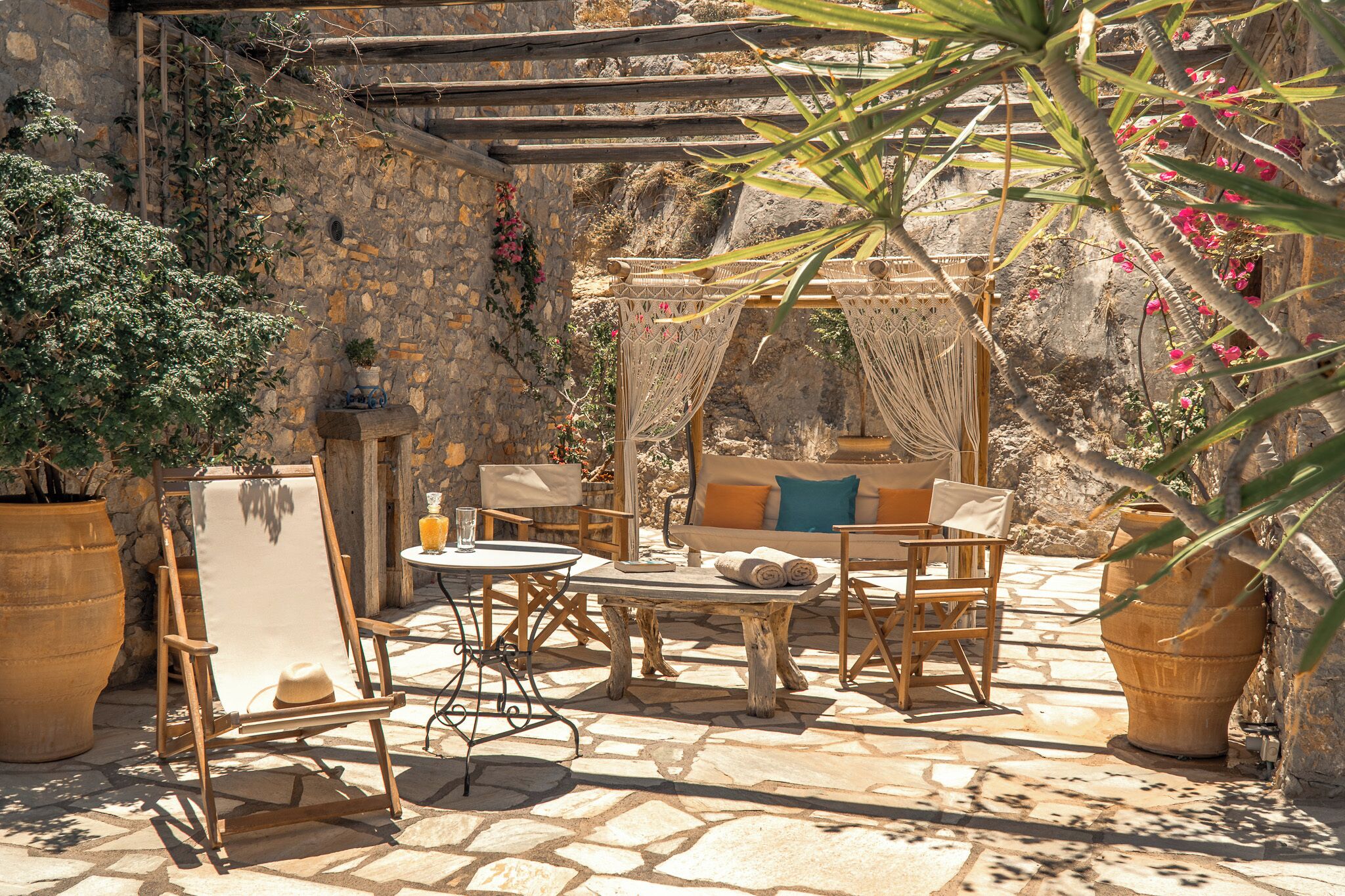 A stone patio with a wooden table and chairs, a hammock, and potted plants.