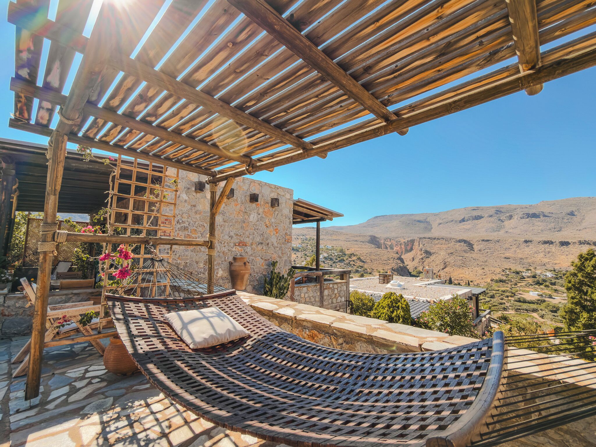 A hammock under a wooden pergola with a stone wall and a view of a valley.