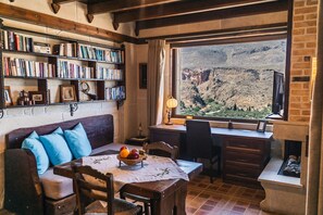 Una habitación acogedora con una estantería, una mesa de comedor con fruteros, un sofá con cojines azules y un escritorio con una lámpara.