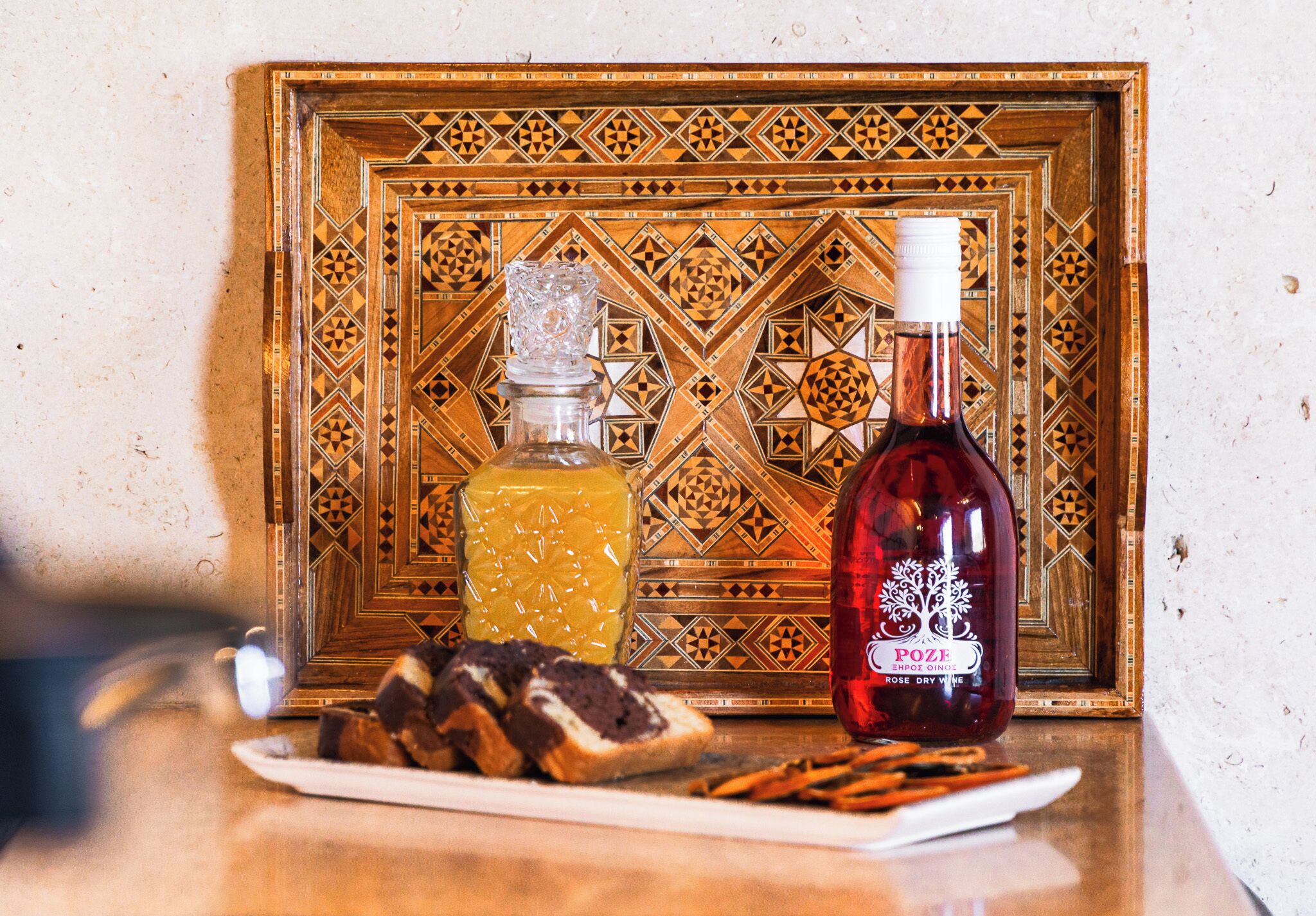 Una botella de vino rosado seco y un vaso de jugo de naranja sobre una mesa con un fondo de azulejos decorativos.