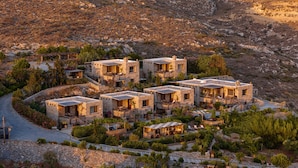 Un conjunto de edificios de piedra con varios balcones, rodeado de vegetación y con montañas al fondo.