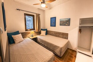 A bedroom with two beds, a window with curtains, a ceiling fan, and artwork on the wall. - Terra Minoika Resort (Sitia)