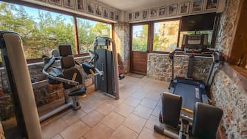 Uma academia com equipamentos de exercício, paredes de pedra e janelas amplas.