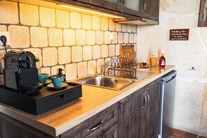 A kitchen with a stone backsplash, a stainless steel sink, a coffee maker, and a dish rack. - Terra Minoika Resort (Sitia)