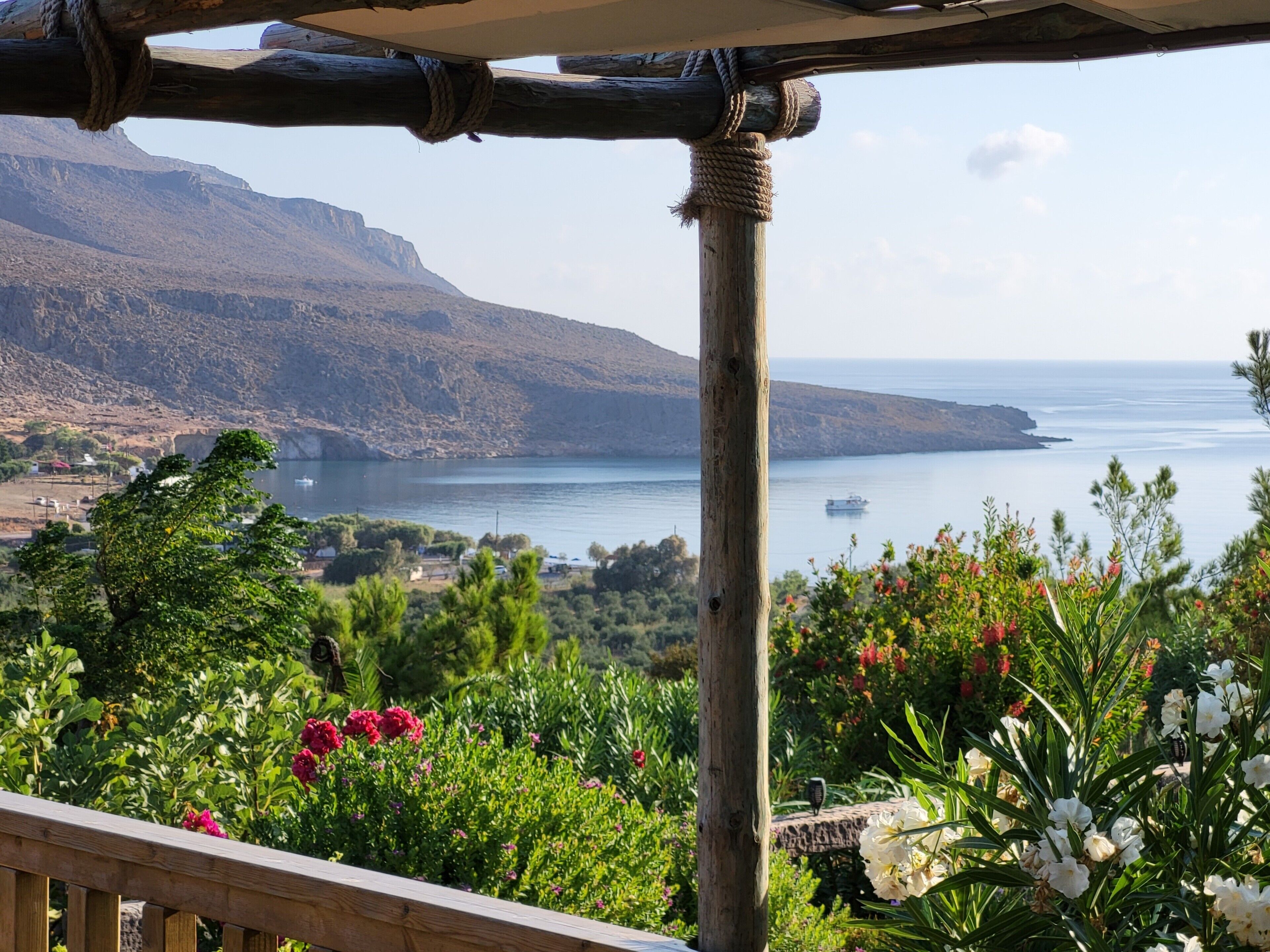 A wooden pergola with a view of a coastal landscape, including a body of water and distant mountains.