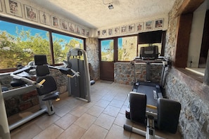A gym with exercise equipment, stone walls, and large windows.