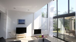 Een moderne woonkamer met een flatscreen televisie, een salontafel en een groot raam met uitzicht op de omgeving.