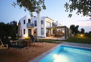 Ein modernes Haus mit Pool, Gartenmöbeln und einer Terrassenfläche.