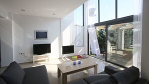 Een moderne woonkamer met een flatscreen televisie, een houten salontafel en een groot raam met uitzicht op de omgeving.