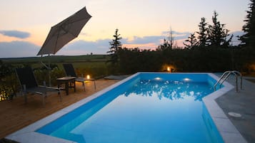 Relax by the serene pool surrounded by lush evergreen trees and a gently sloping field.