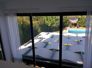 Vista desde una ventana sobre una zona de piscina con sombrillas y sillas de descanso.