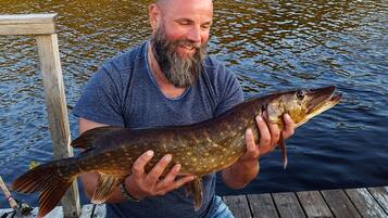 Un hombre sostiene un pez en un muelle de madera junto a un lago.