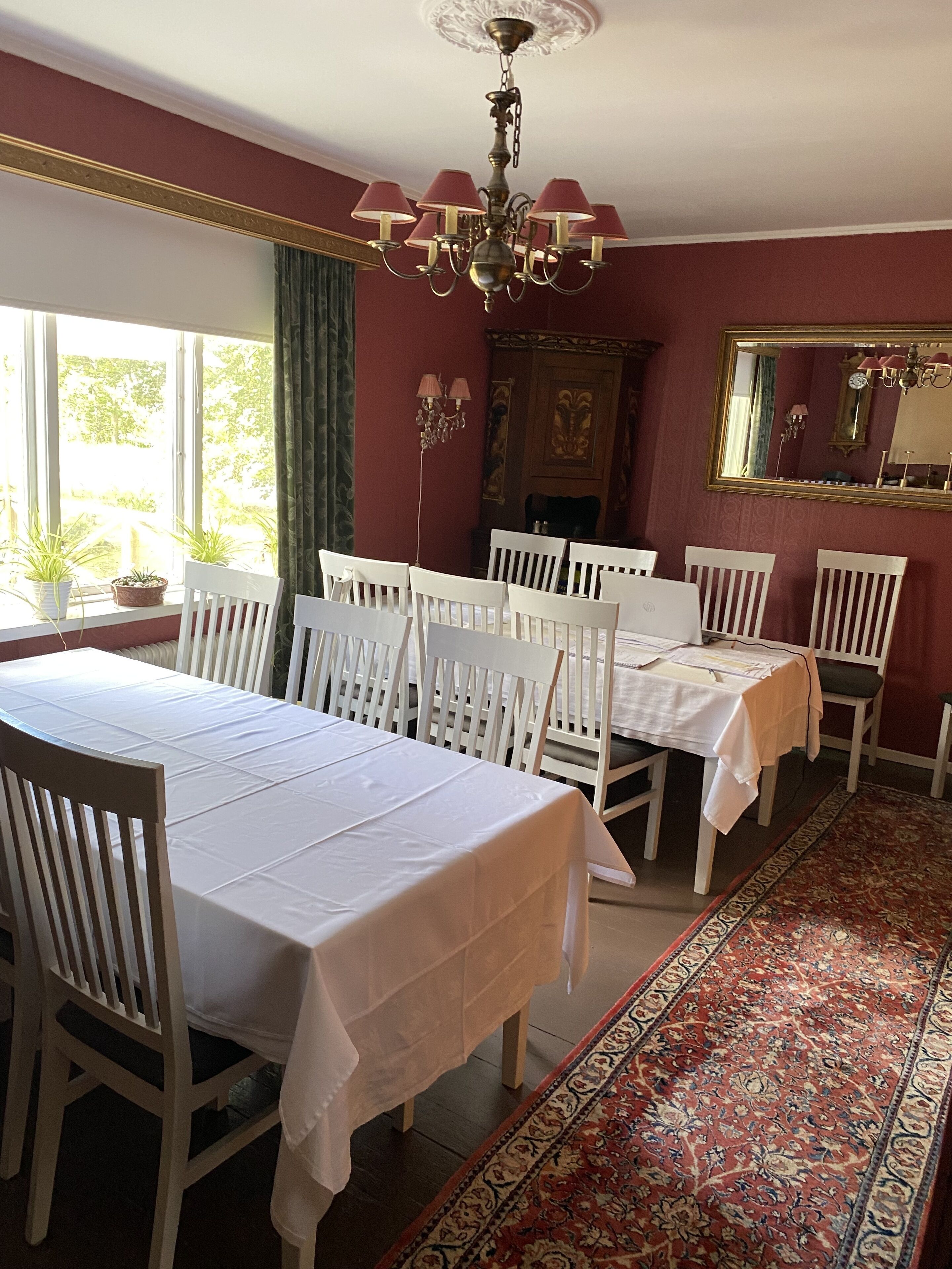 A dining room with two white tables and chairs, a chandelier, a large mirror, and a patterned rug.