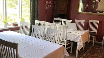 A dining room with two white tables and chairs, a chandelier, a large mirror, and a patterned rug.