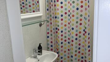 Une salle de bain avec un lavabo blanc, une étagère en verre au-dessus et un rideau de douche à pois colorés.