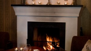 A cozy room with a fireplace, a candelabra, and a table set with a glass of wine, a cup, and a plate. - Wärdshuset Furuliden (Vittsjo)