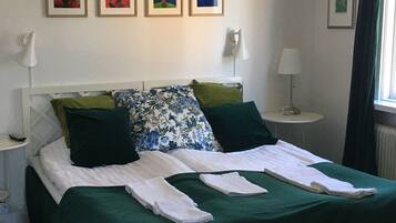 Una cama bien hecha con ropa de cama verde, dos mesitas de noche con lámparas y cuatro cuadros enmarcados en la pared.