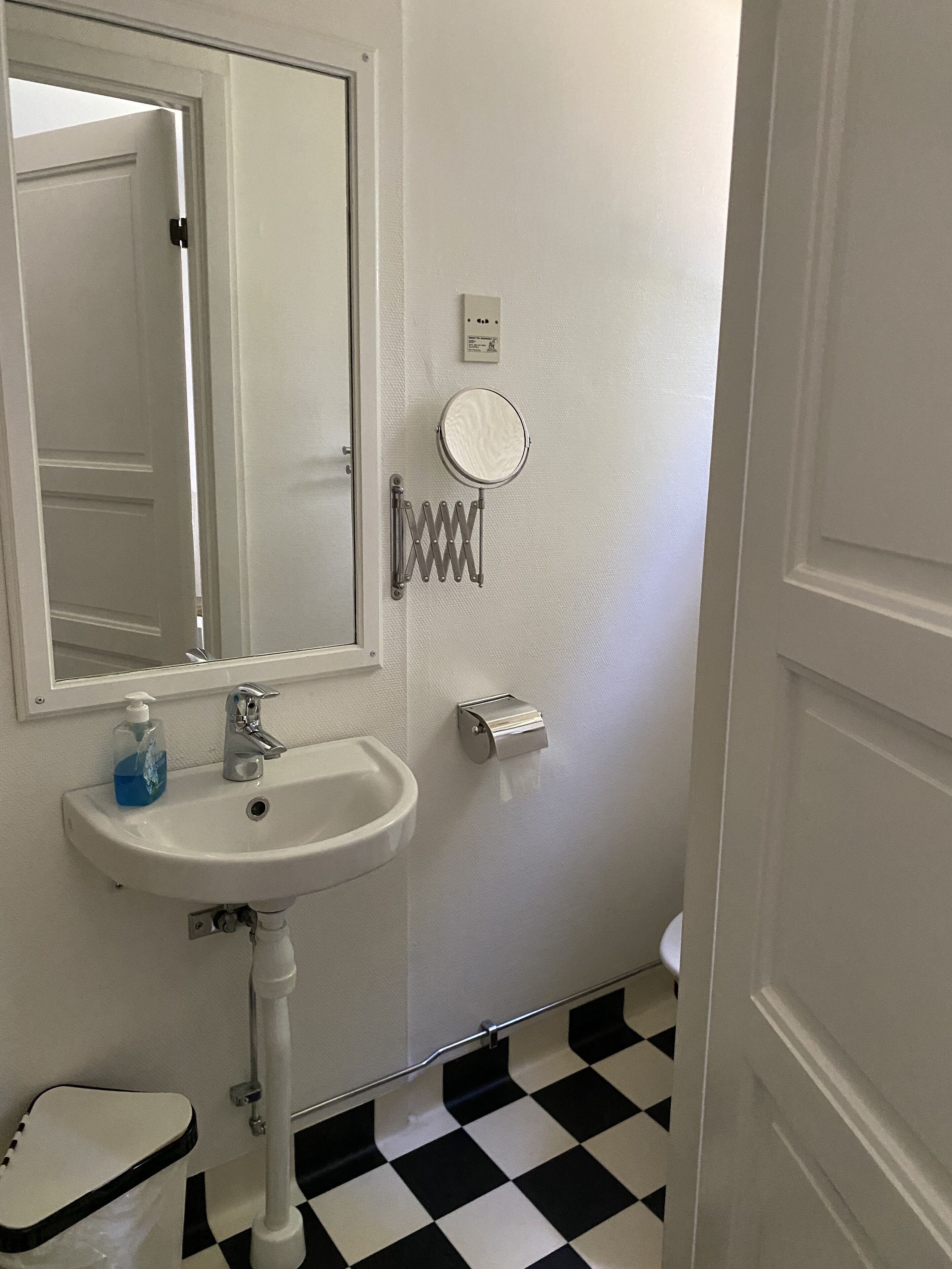A bathroom with a white sink, a mirror, a toilet, and a black and white checkered floor.