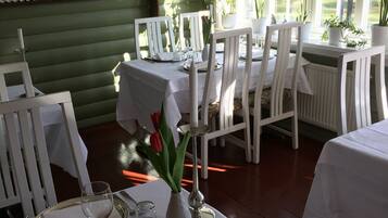 A dining area with white tables and chairs, a green wall with decorative plates, and a window with plants.