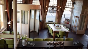 Un restaurant avec une longue table en bois, des chaises vertes et une vue sur la ville grâce à de grandes fenêtres.