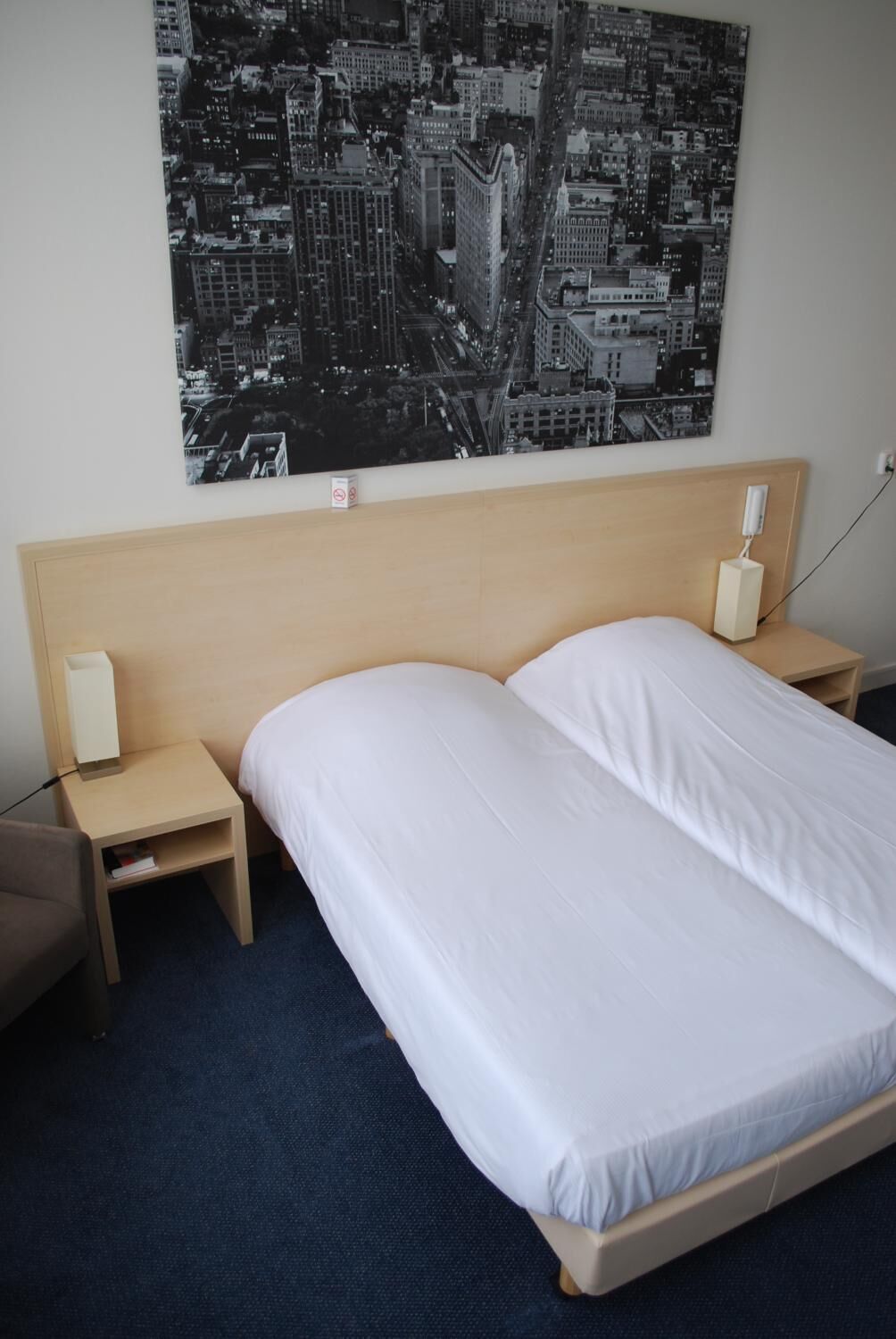Een hotelkamer met een groot bed, twee nachtkastjes, een wandtelefoon en een poster van een stadsgezicht.