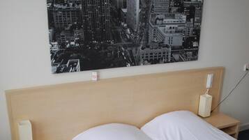 Een hotelkamer met een groot bed, twee nachtkastjes, een wandtelefoon en een poster van een stadsgezicht.