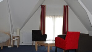 Une pièce avec un plafond en pente, un lit, une petite table, deux chaises et une fenêtre avec des rideaux.