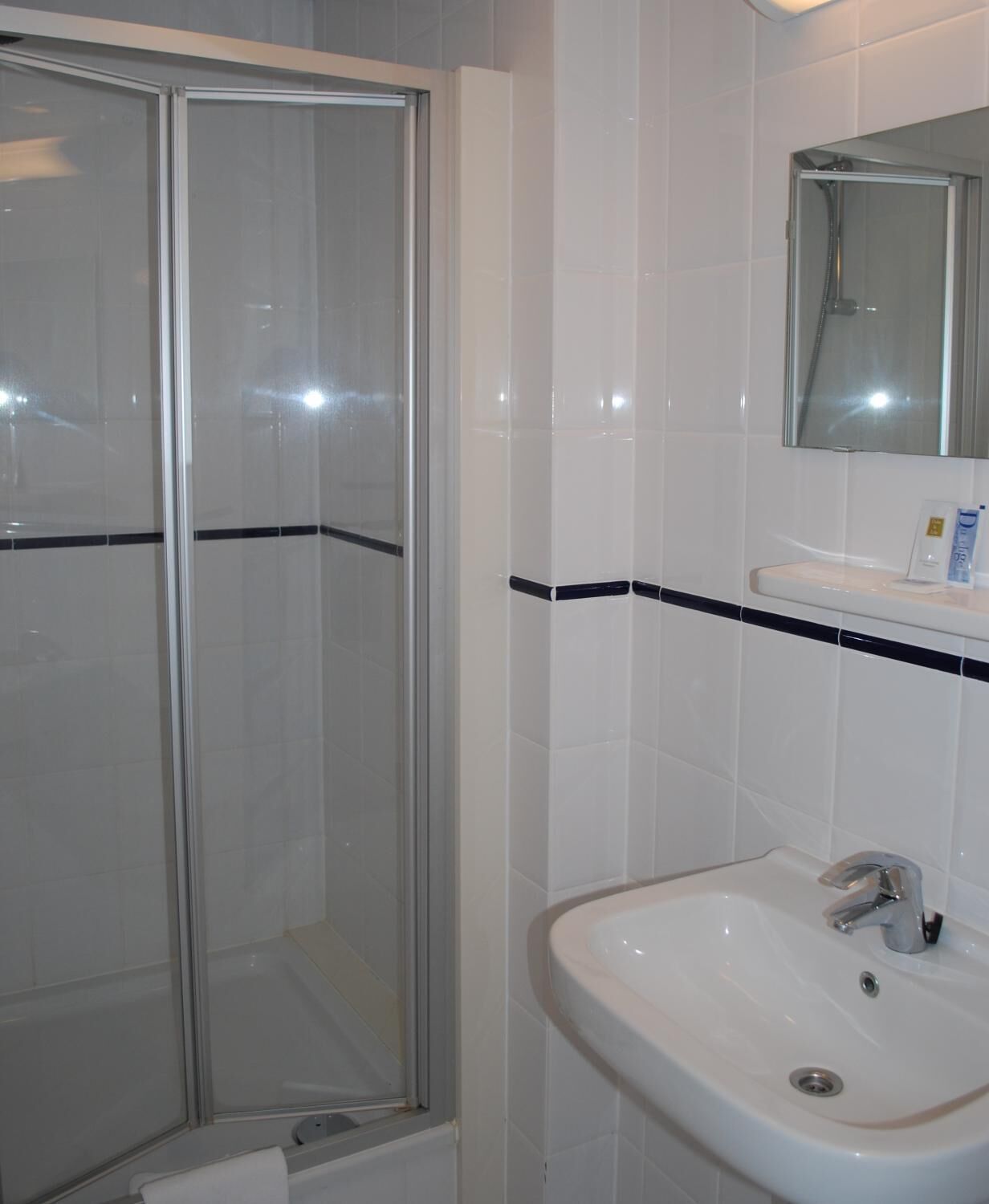 Une salle de bain avec une douche à parois de verre, un lavabo blanc doté d’un seul robinet et un miroir au-dessus du lavabo.