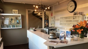 Un espace d’accueil avec un comptoir blanc, une horloge, un présentoir à clés et un vase de fleurs.