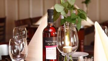 Una mesa con una botella de vino Santa Ana, dos copas de vino vacías, una vela y un florero con rosas.