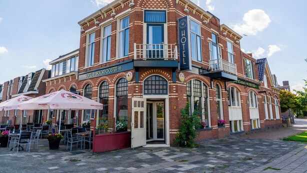 Un hôtel historique avec une entrée située à l’angle de l’immeuble, des places assises en plein air et une enseigne bien visible.