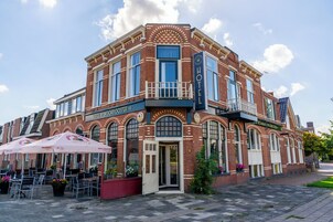 Um hotel histórico com entrada de esquina, área de estar ao ar livre e placa chamativa.