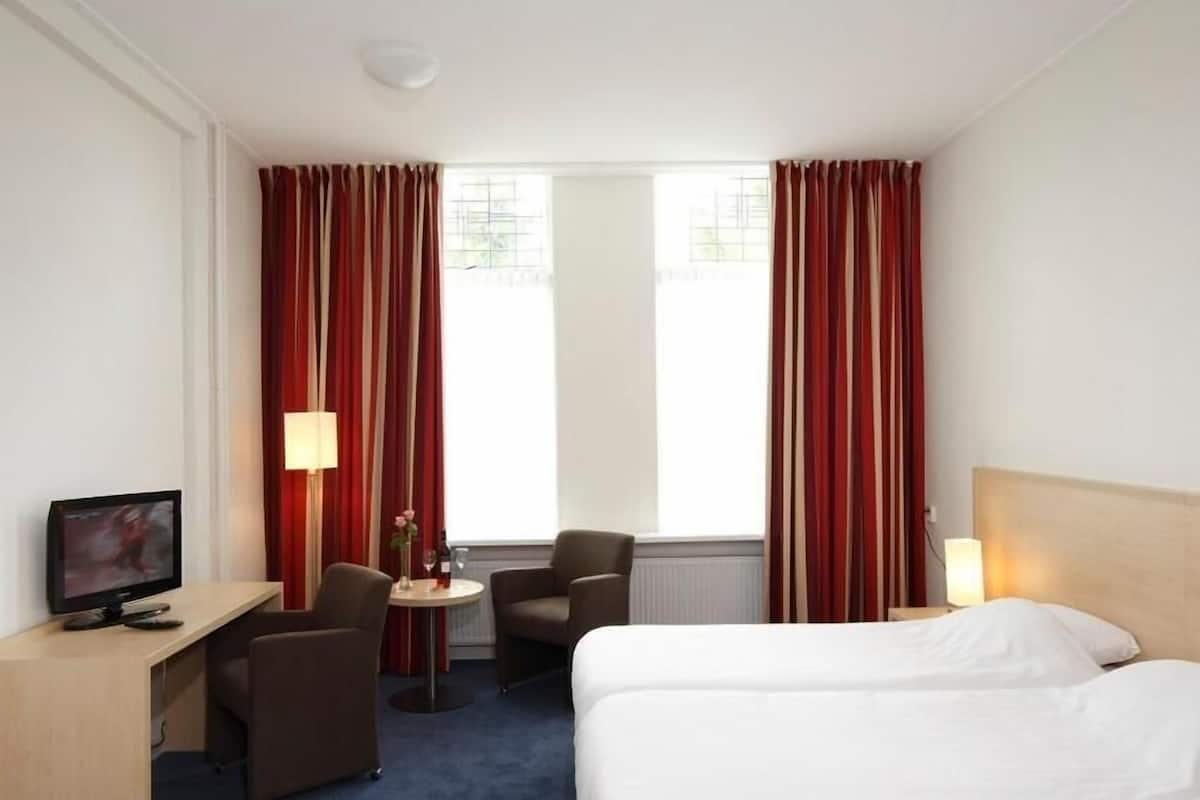 Habitación de hotel con cama, escritorio con computadora, silla y pequeña mesa con lámpara.