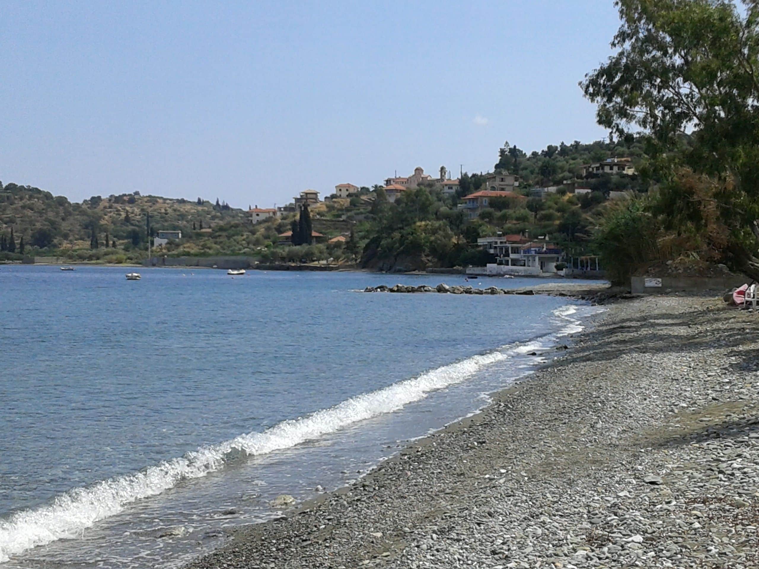 Une plage de galets offrant une vue dégagée sur la mer et une colline parsemée de bâtiments.