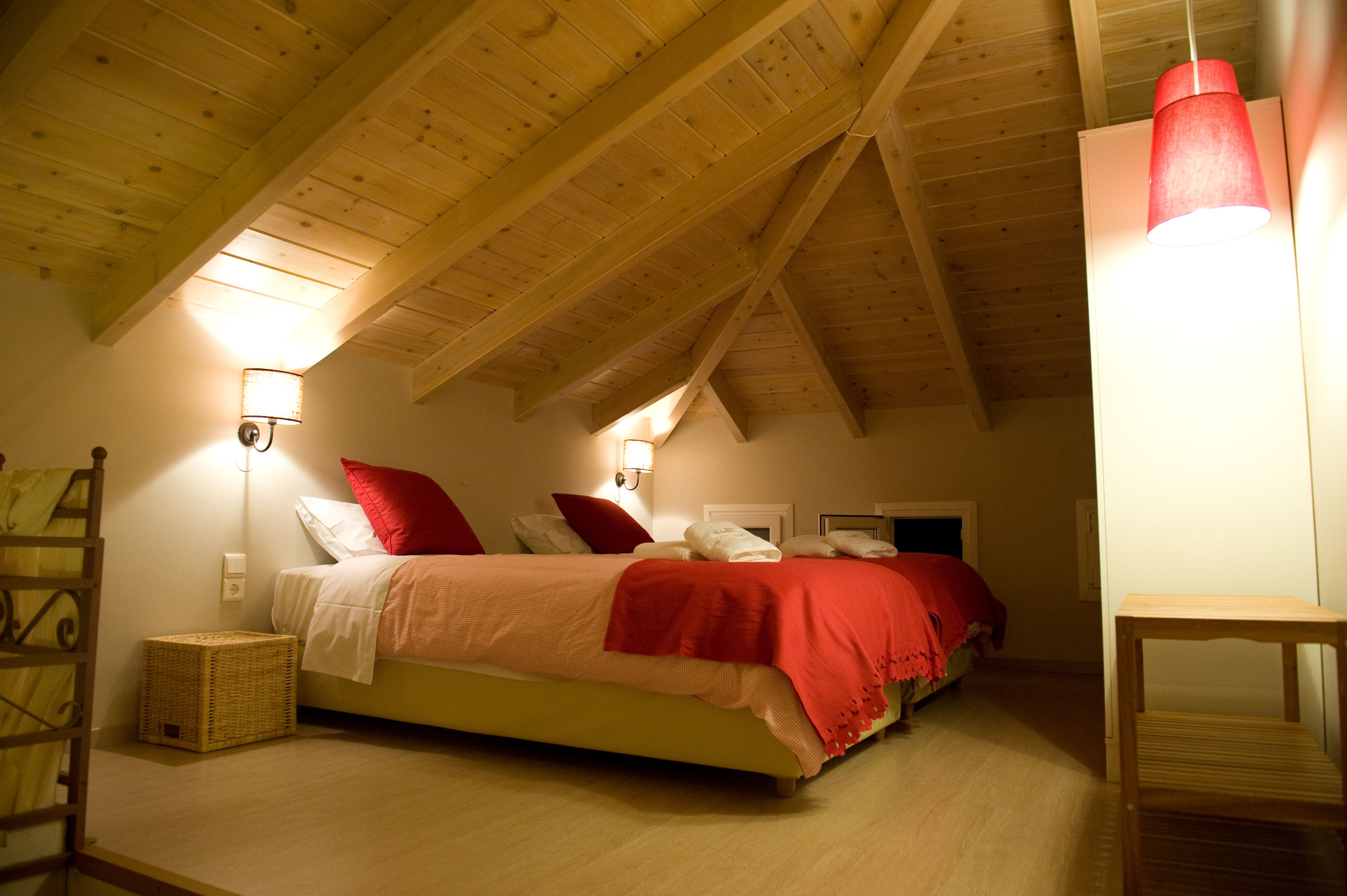 A bedroom with a sloped ceiling, a bed with red and white bedding, a wooden headboard, and a small table.