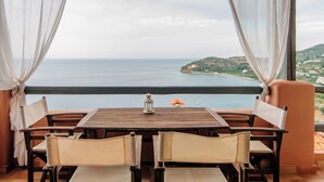 Ein Essbereich mit Tisch und Stühlen, Blick auf das Meer und eine bergige Landschaft im Hintergrund.