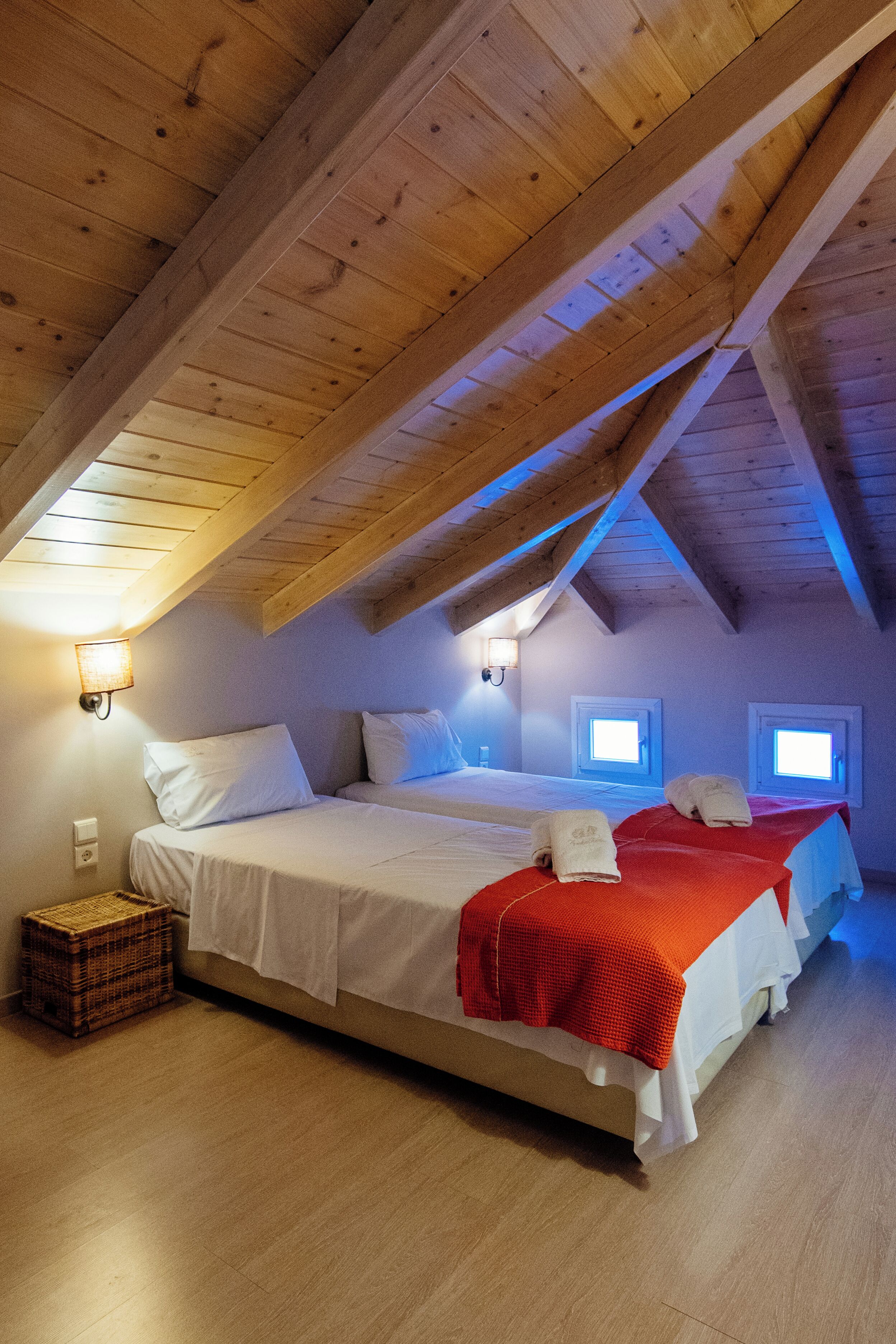 A bedroom with two beds, wooden beams, a wall-mounted light, and a small window.