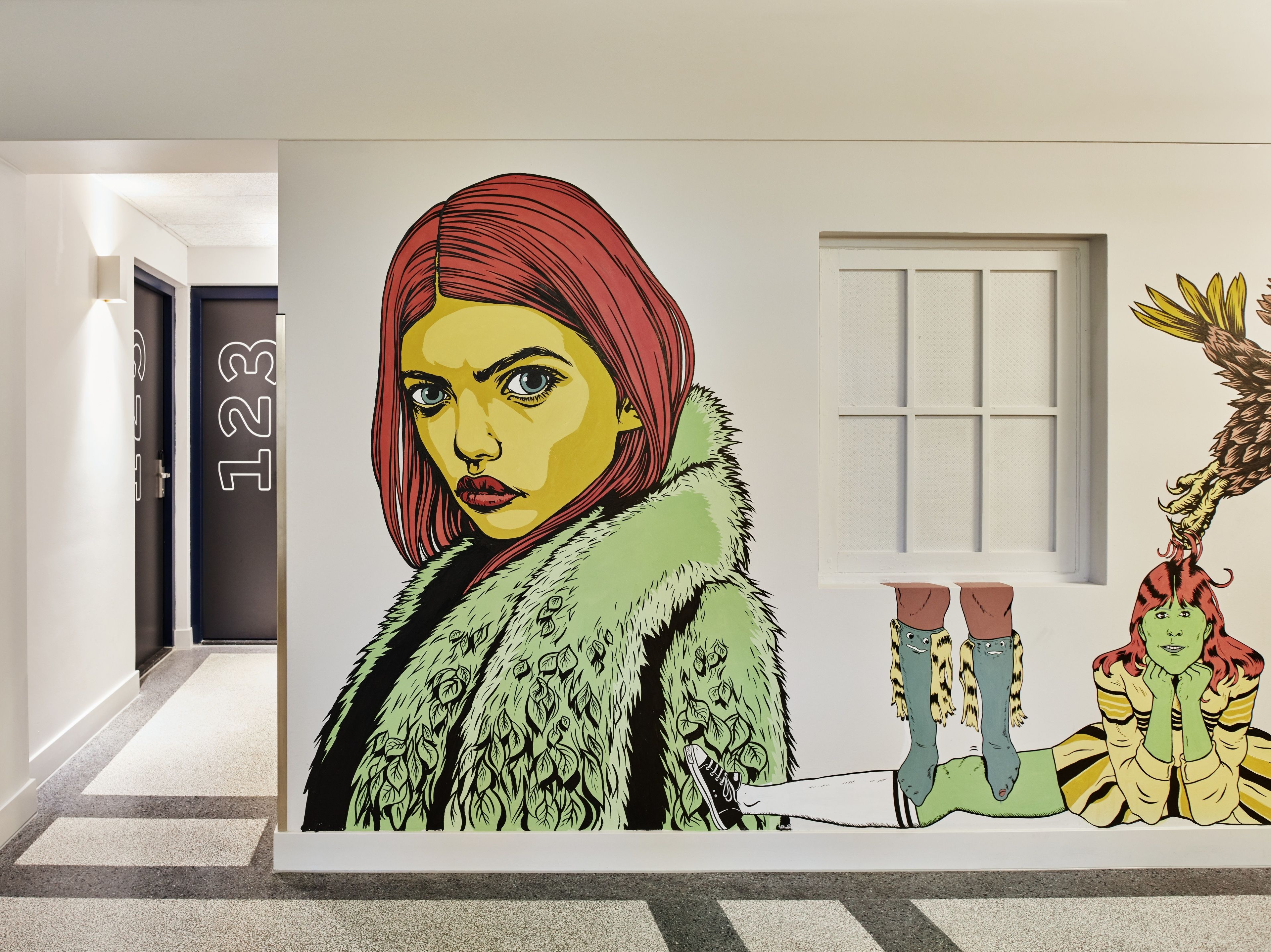 Un pasillo con un gran mural que muestra a una persona con abrigo de piel, una criatura verde y un personaje pelirrojo.