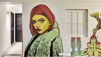 Un pasillo con un gran mural que muestra a una persona con abrigo de piel, una criatura verde y un personaje pelirrojo.