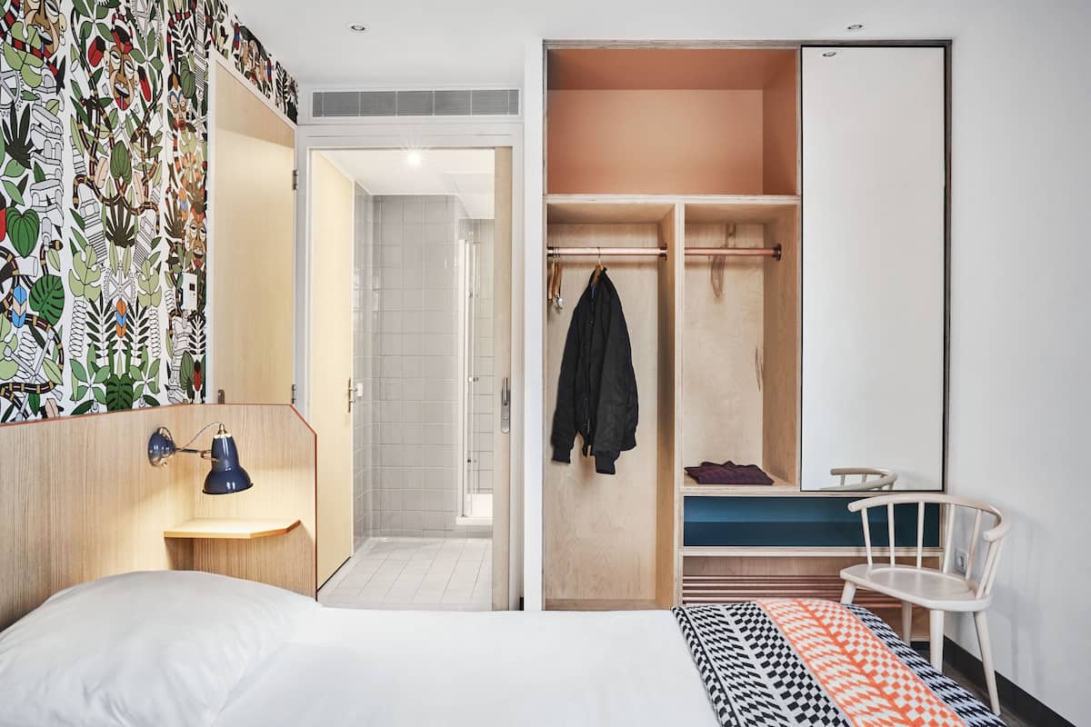 Une chambre d’hôtel comprenant un lit, un bureau avec une lampe, une armoire et un espace douche.