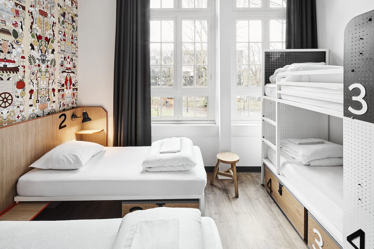 Une chambre d’hôtel moderne dotée d’une grande fenêtre, d’un mur orné d’un motif coloré et d’un lit superposé avec le chiffre « 3 » sur le côté.