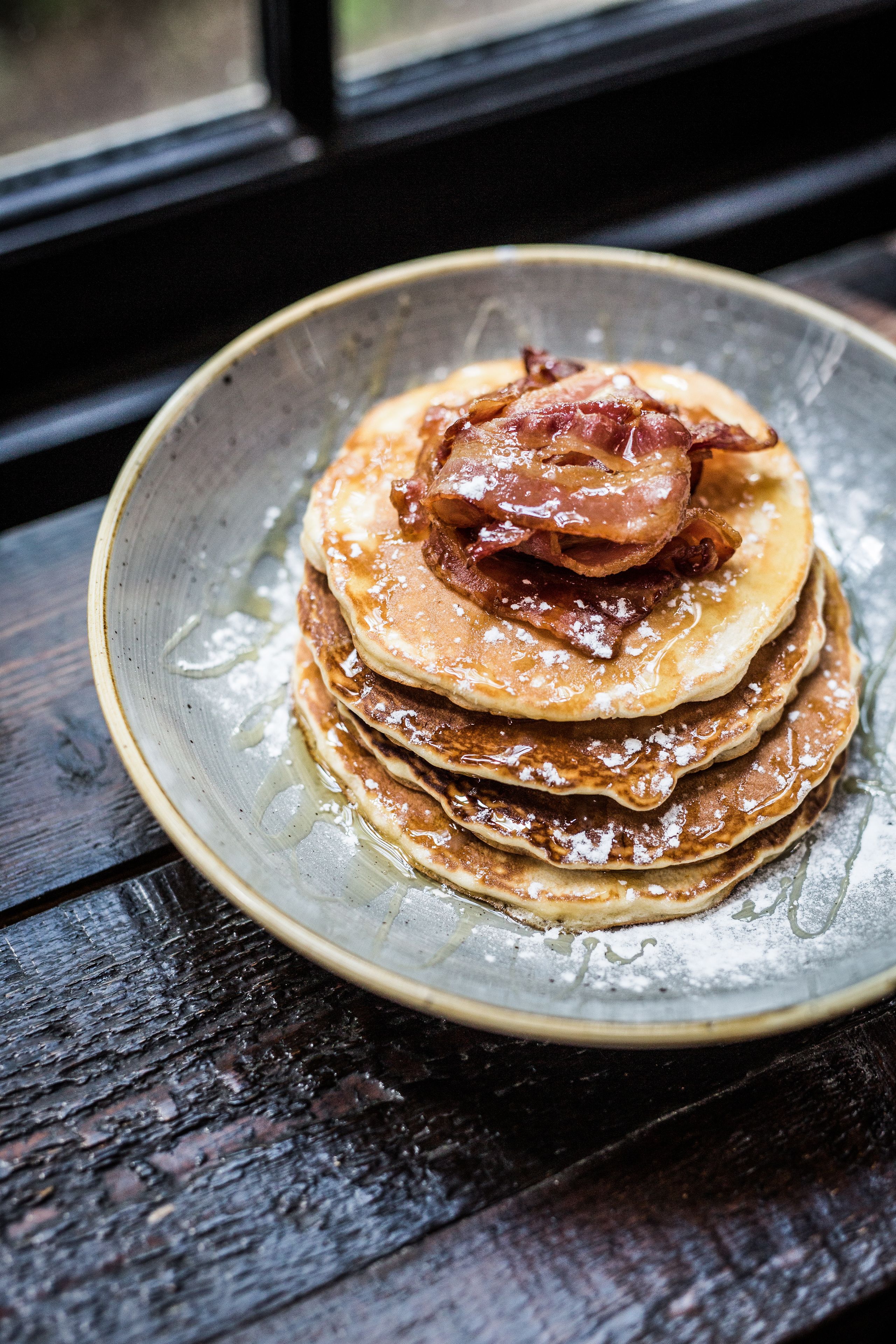 Una pila de tortitas con almíbar y tocino sobre un plato de cerámica.