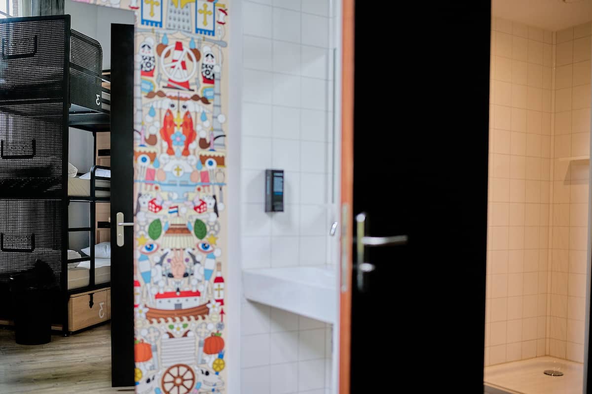 Une pièce avec un lit superposé, un mur coloré orné de divers motifs, un lavabo blanc et une porte noire.