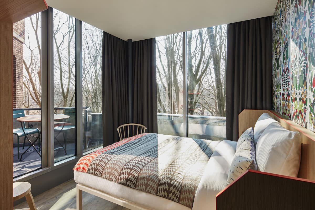 Une chambre moderne avec une grande fenêtre, un lit en bois et une vue sur l’extérieur.