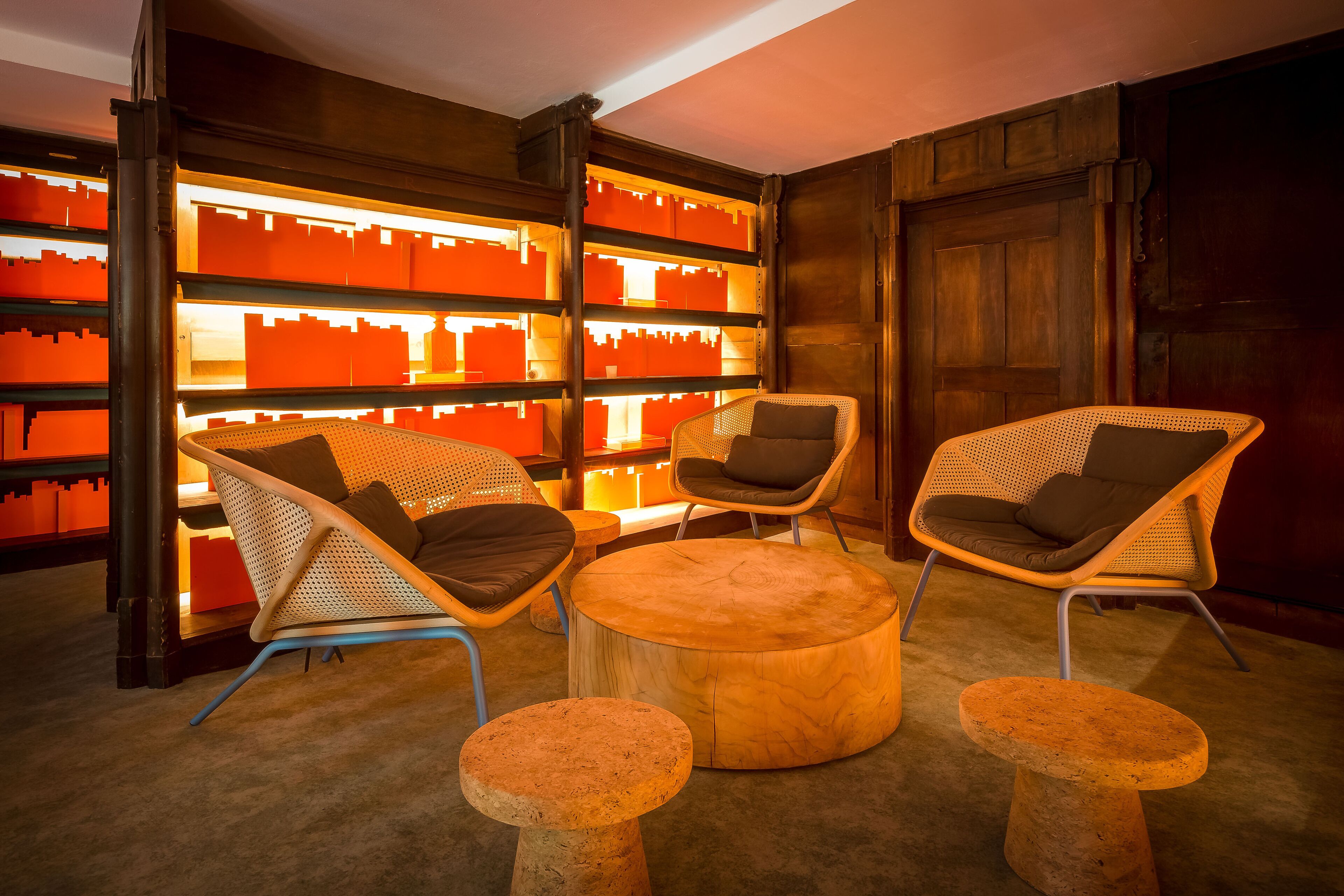 Ein gemütlicher Sitzbereich mit Korbstühlen und einem runden Holztisch, umgeben von einer Bücherwand mit beleuchteten, orangefarbenen Elementen.