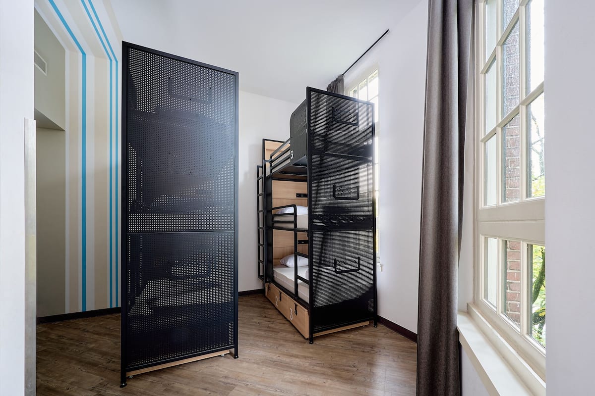 Une chambre avec un lit superposé, une cloison en métal noir et une fenêtre donnant sur l’extérieur.