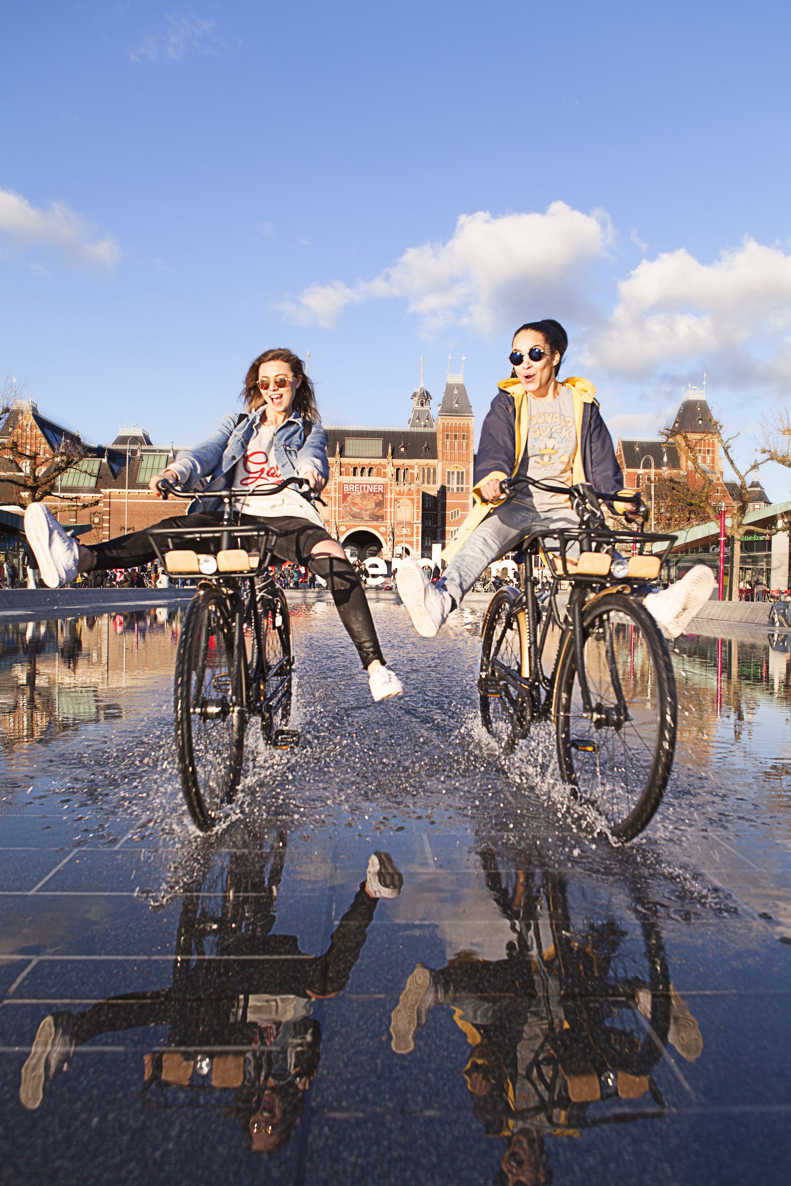 Two people on bicycles in a puddle with a historic building in the background.